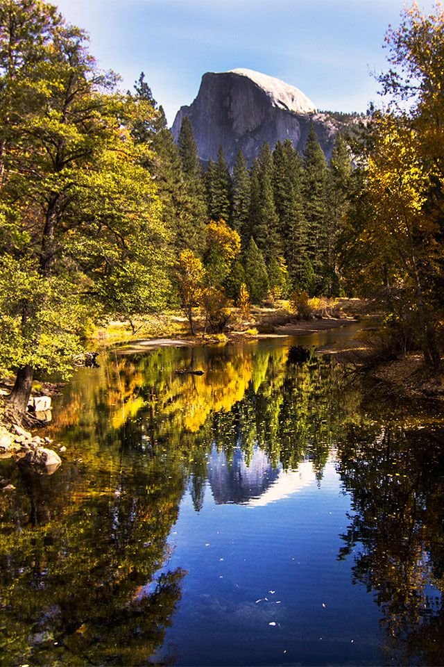 This may contain: a mountain is reflected in the still water of a river with trees and rocks around it