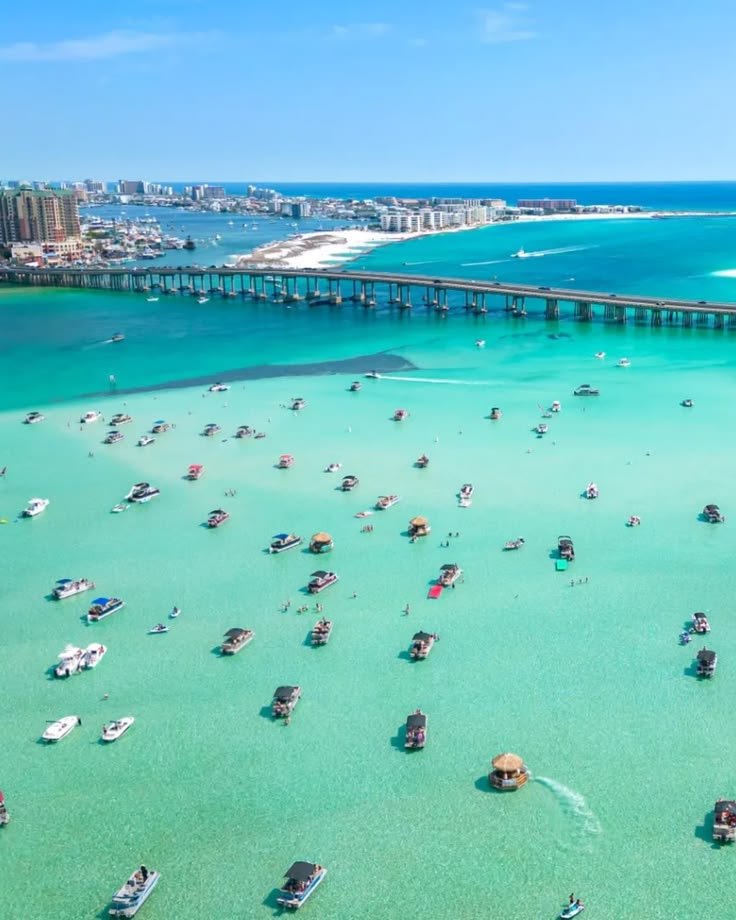 This may contain: many boats are in the water near a pier and beach with a bridge over it