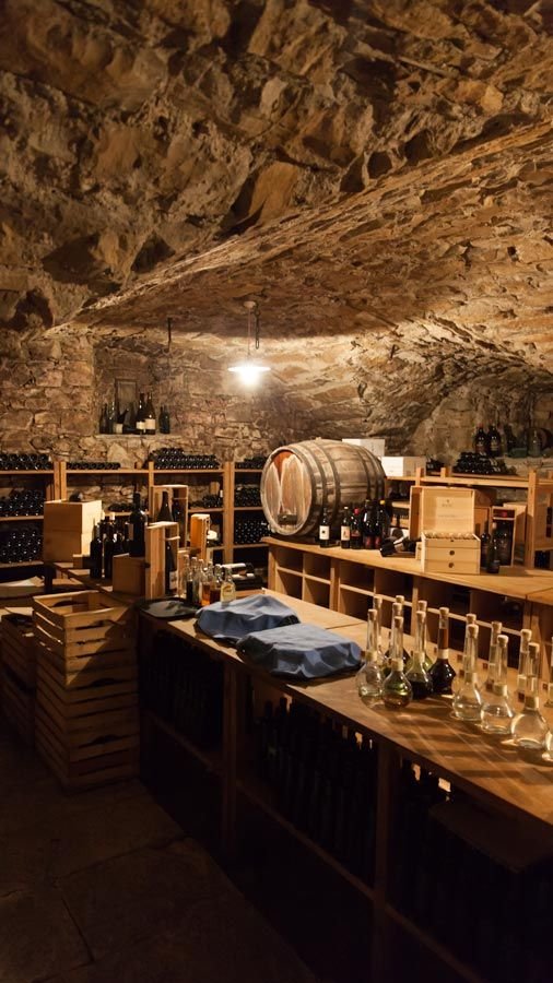 This may contain: a wine cellar filled with lots of bottles and glasses on top of wooden shelves under a cave like ceiling