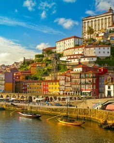 This may contain: boats are docked on the water in front of colorful buildings and cliffs, with blue sky above