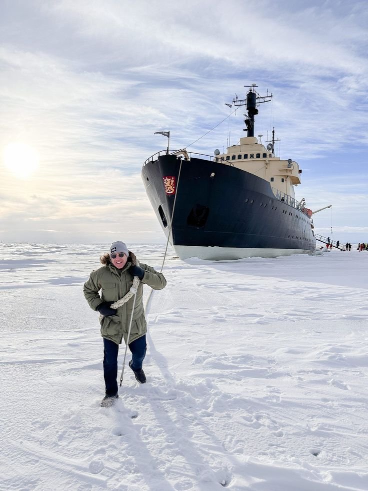 This may contain: a person standing in the snow with a large boat behind them on top of ice