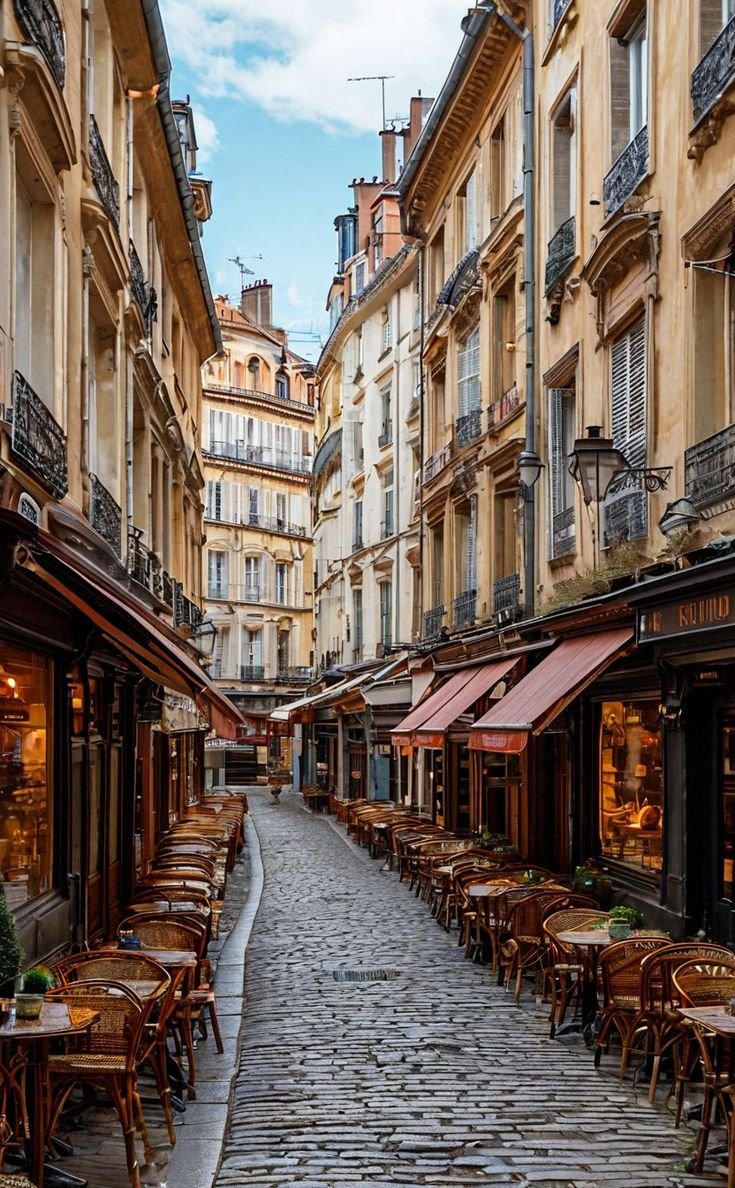 This may contain: an empty street with tables and chairs in the middle, lined with tall buildings on both sides