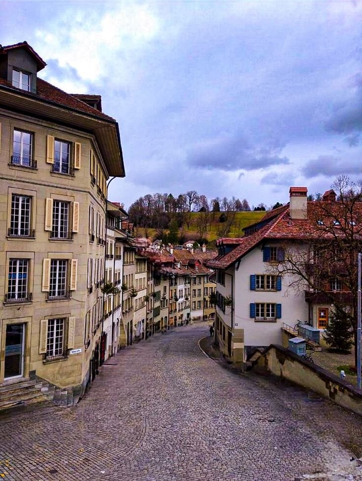 This may contain: an empty street with several buildings on both sides and cobblestone pavement in the middle