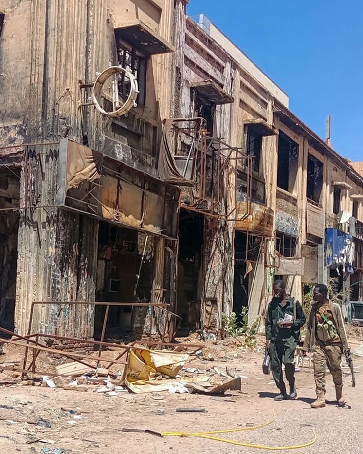 This may contain: two men walking down the street in front of an old building that has been destroyed