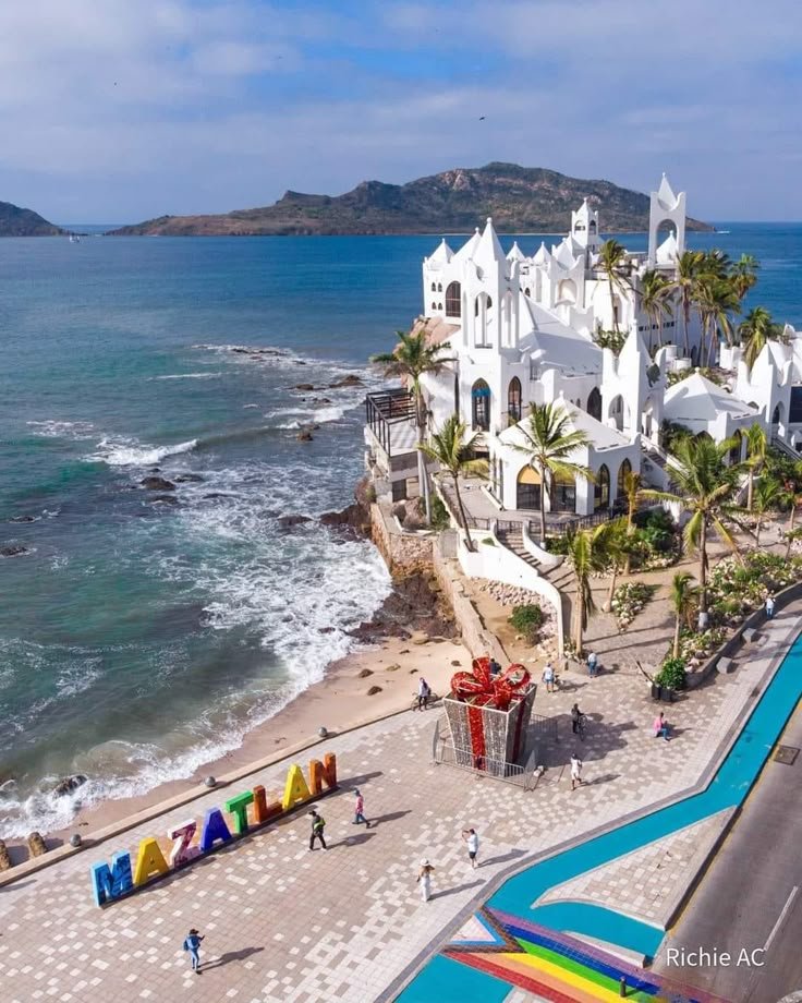 This may contain: an aerial view of the beach and ocean in front of a white building with colorful letters