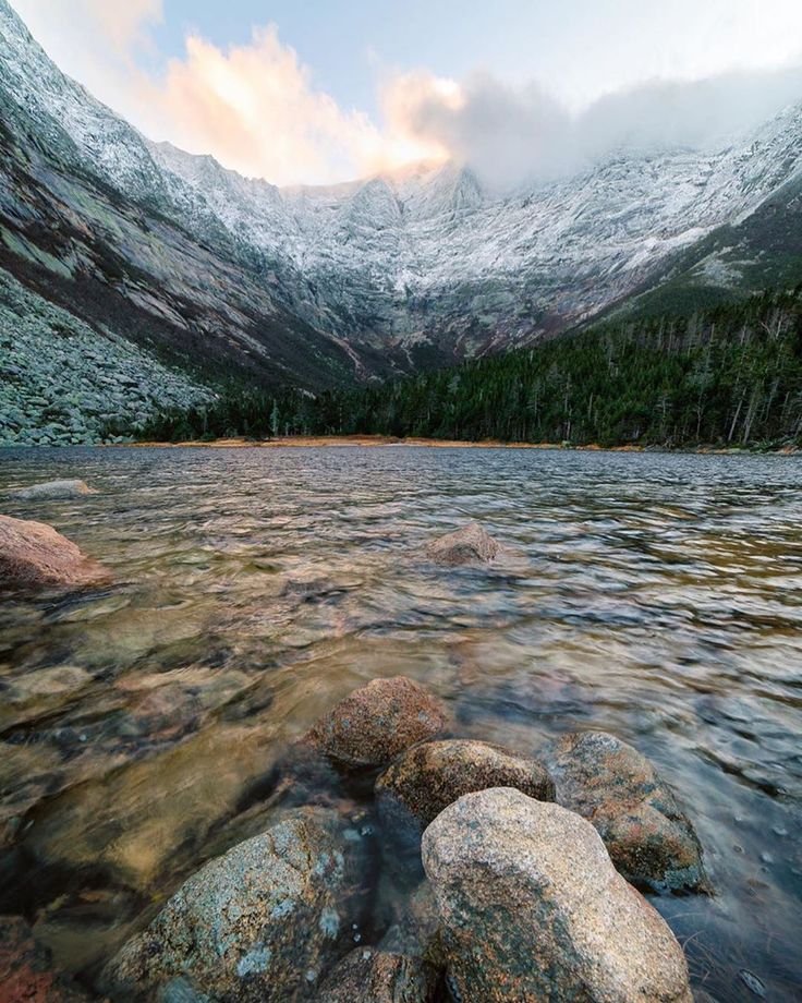 This may contain: some rocks in the water and snow covered mountains