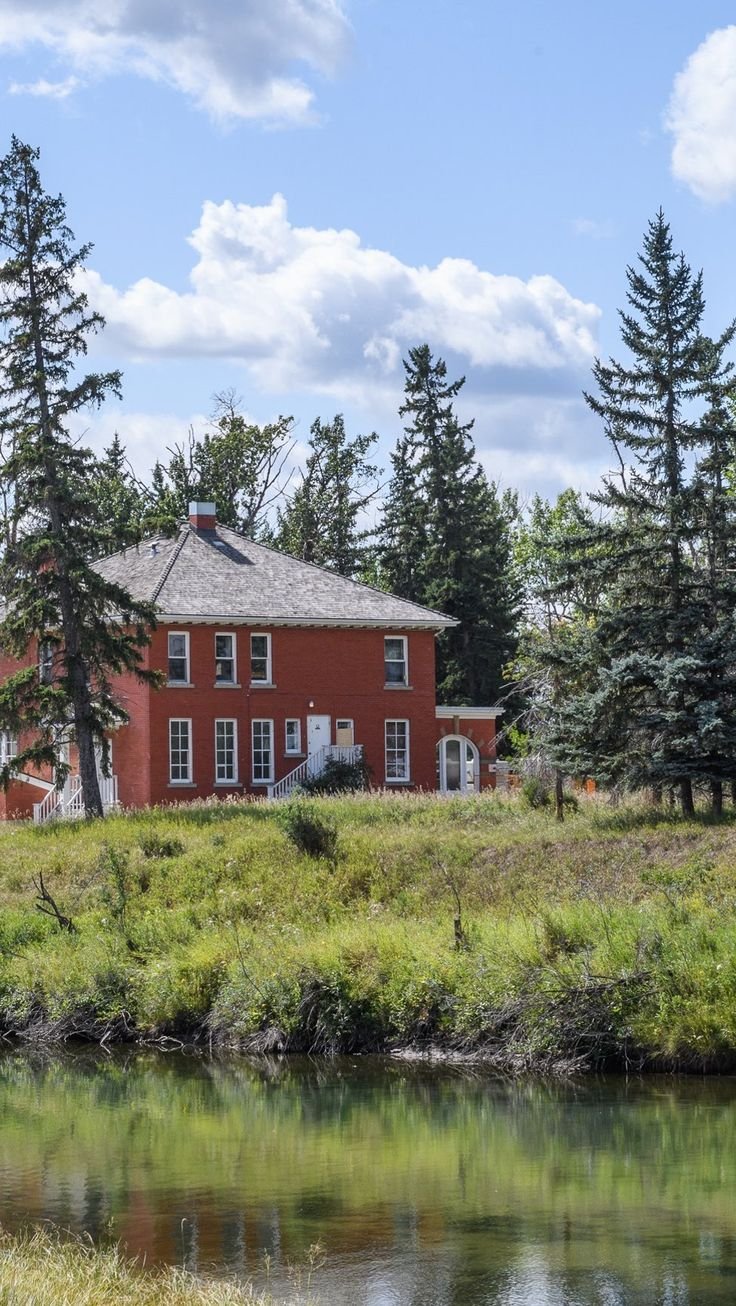 This may contain: a red house sitting on top of a lush green field next to a river and forest
