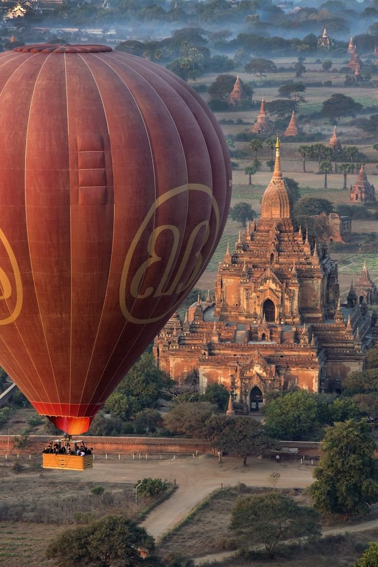 This may contain: a hot air balloon flying in the sky over a large city with many spires