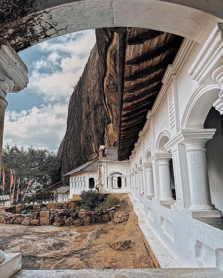 This may contain: an arch in the side of a building with stone steps leading up to it and a mountain behind