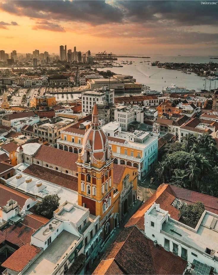 This may contain: an aerial view of a city with tall buildings and water in the background at sunset