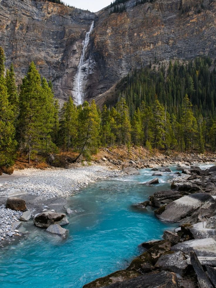 This may contain: a river with blue water surrounded by trees and mountains in the background, near a waterfall