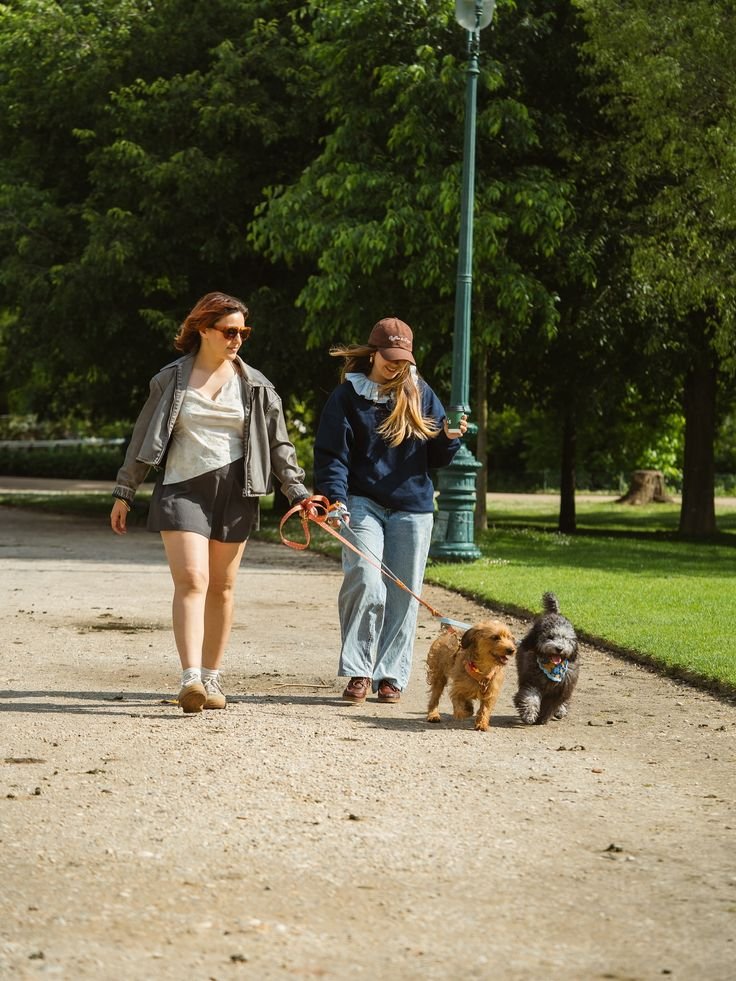 This may contain: two women walking their dogs on a path in the park, one with a leash
