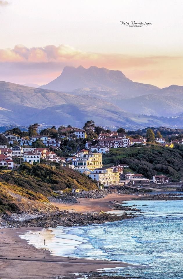 This may contain: a beach with houses on the shore and mountains in the background