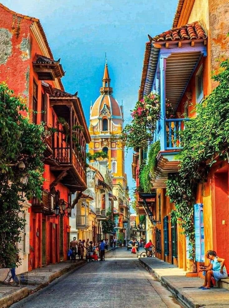 This may contain: an empty street with people sitting on the benches and buildings in the backround