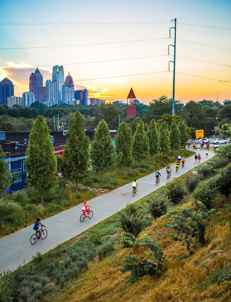 This may contain: many people are riding bikes down the road in front of some tall buildings and trees