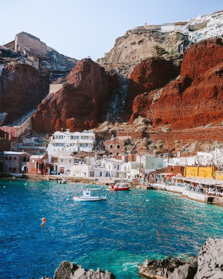 This may contain: the water is blue and clear with boats in it near some buildings that are red cliffs