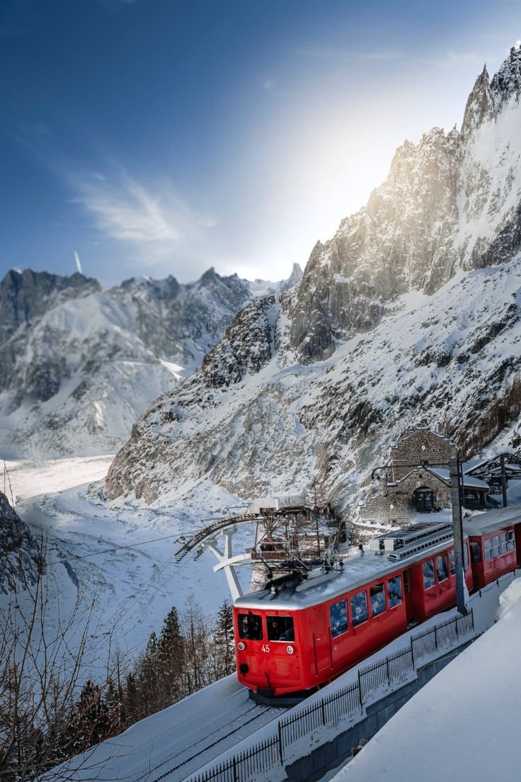 This may contain: a red train traveling down tracks next to snow covered mountain side under a blue sky