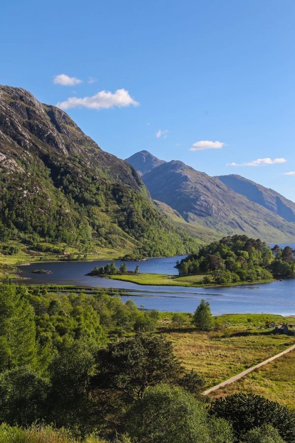 This may contain: a lake surrounded by mountains in the middle of a green field with trees and bushes