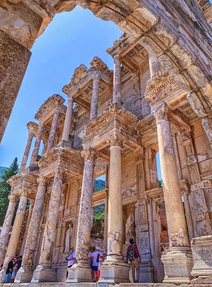 This may contain: people are standing in front of an old building with columns and stone carvings on it