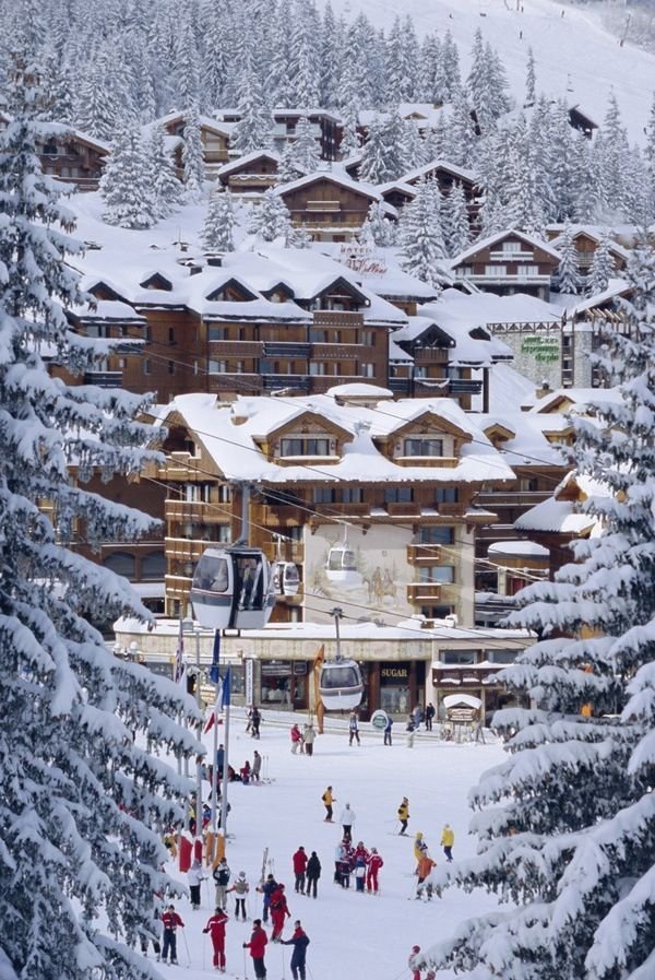 This may contain: a ski lodge surrounded by snow covered trees and people skiing on the slopes in front of it