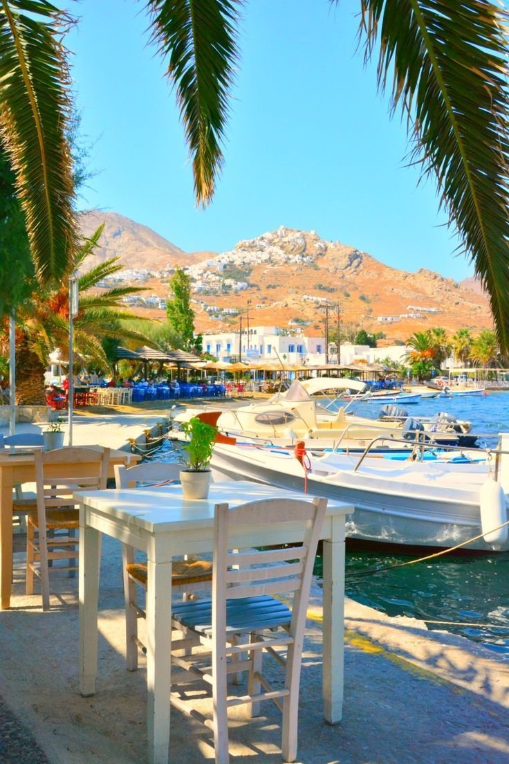 This may contain: there is a table and chairs on the beach next to the boats in the water