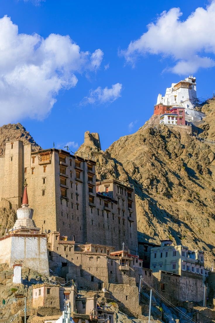 This may contain: an old building on the side of a mountain with clouds in the sky above it