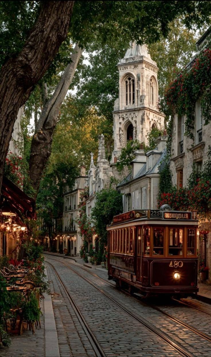 This may contain: an old fashioned trolley is going down the street in front of some buildings and trees