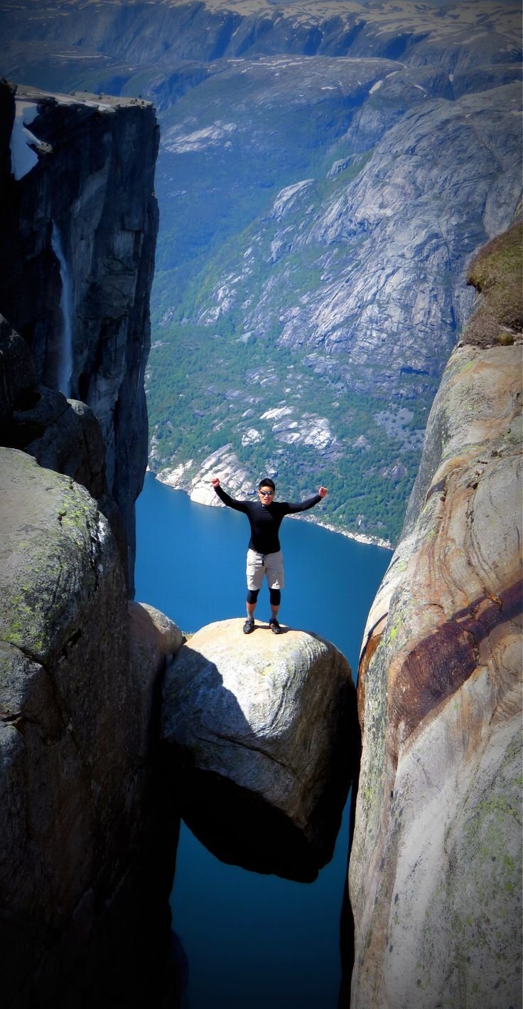 This may contain: a man standing on top of a large rock next to a body of blue water