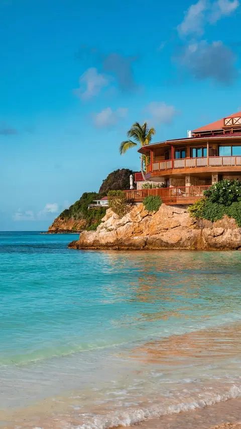 This may contain: a house sitting on top of a beach next to the ocean