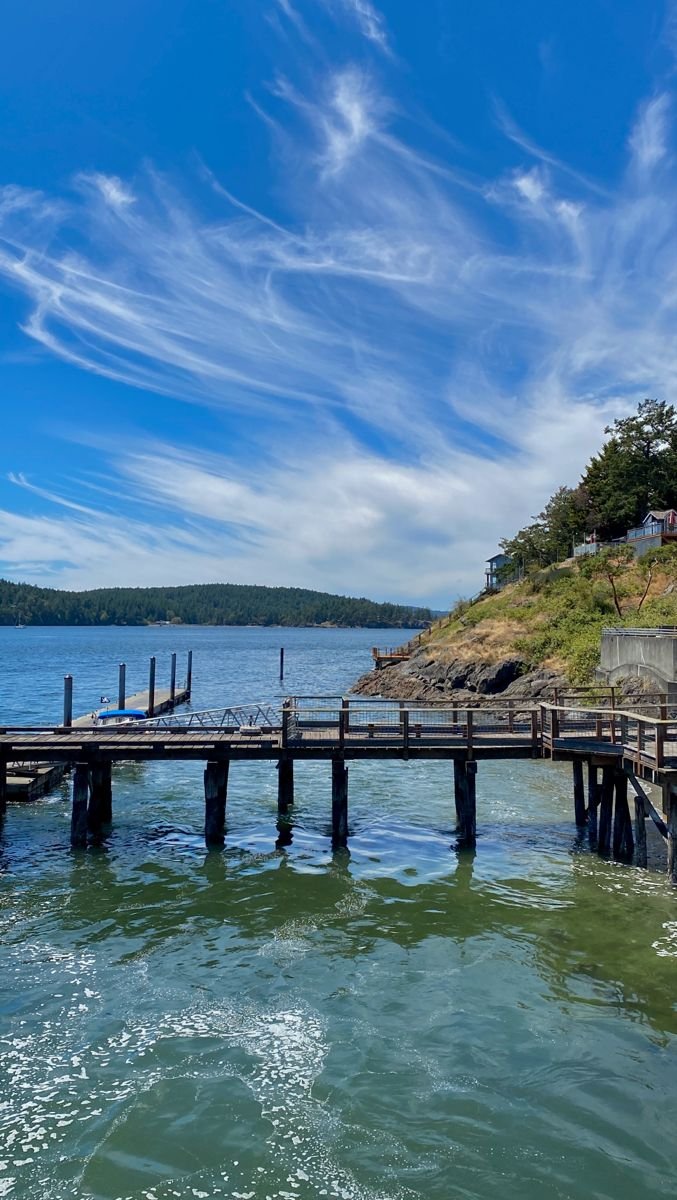 This may contain: a pier on the edge of a body of water under a blue sky with wispy clouds