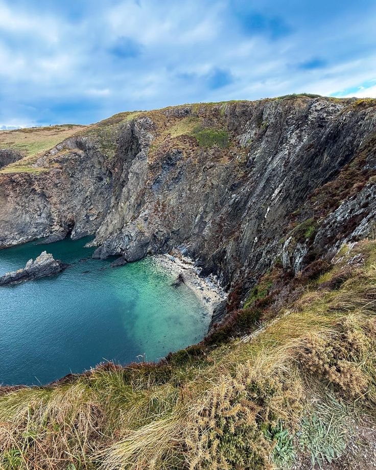 This may contain: the water is very blue and green in this mountain side area with cliffs on both sides