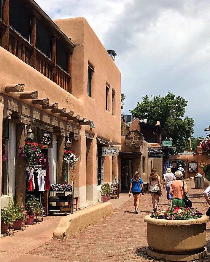 This may contain: people walking down the street in front of shops with flower pots and potted plants