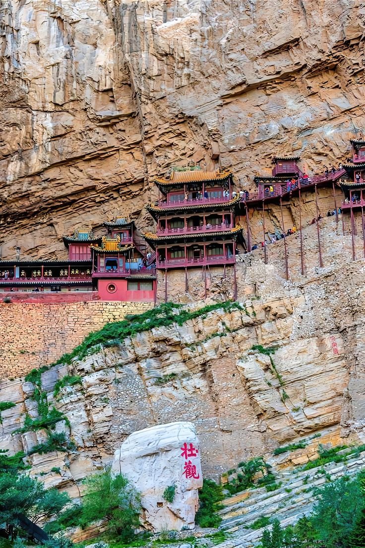 This may contain: the building on the side of the mountain is red and black with writing in chinese