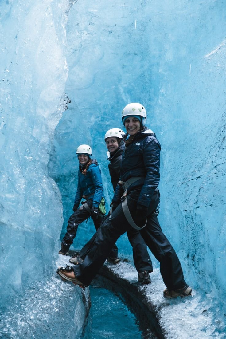 This may contain: three people standing in an ice cave