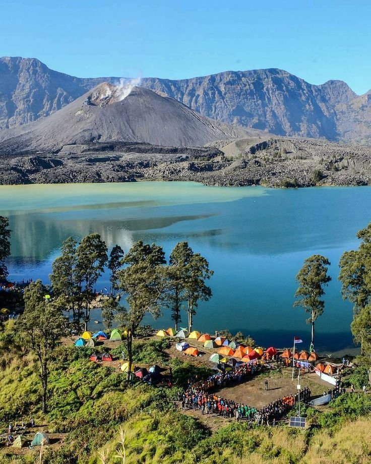 This may contain: a group of people standing on top of a lush green hillside next to a lake