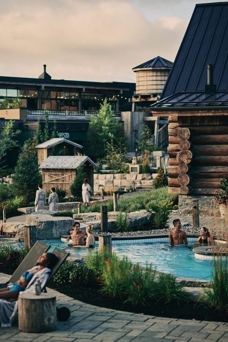 This may contain: people are relaxing in the hot tubs at an outdoor swimming pool with log buildings