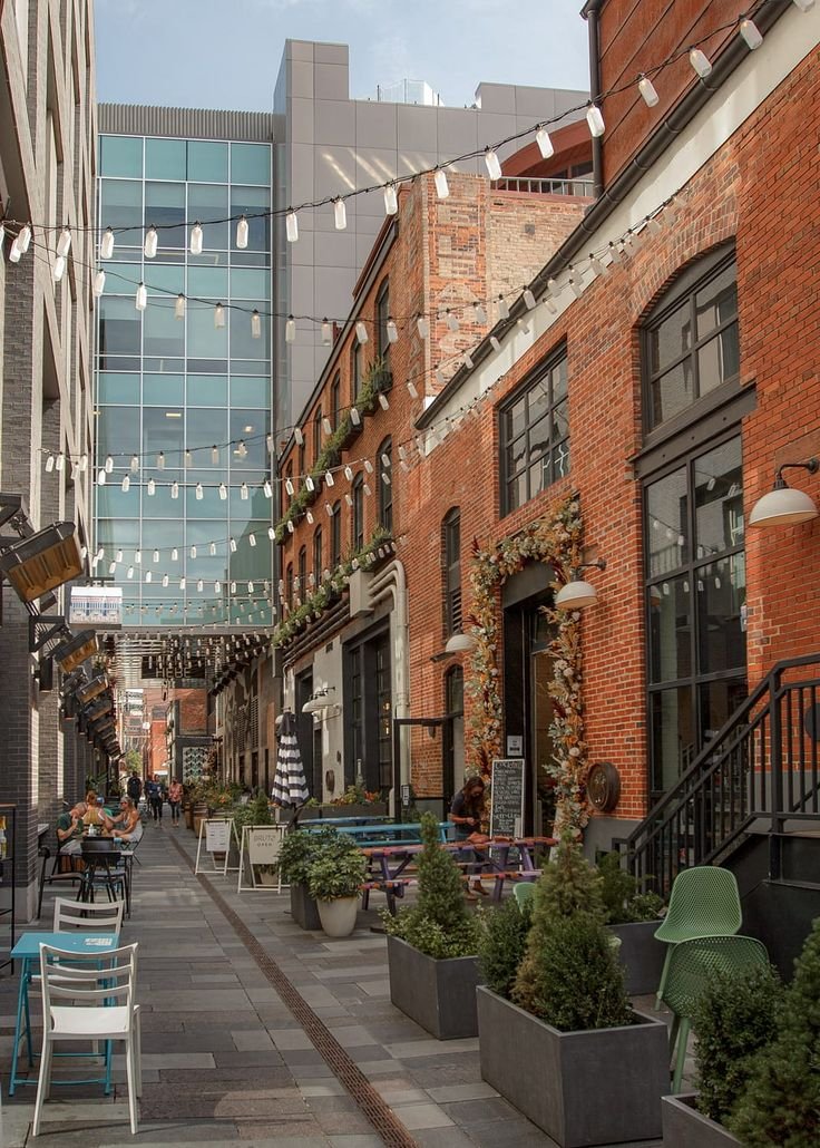 This may contain: an empty city street with tables and chairs on both sides, surrounded by tall buildings