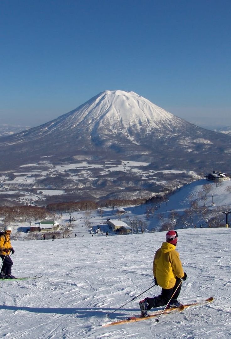 This may contain: two people on skis in the snow with a mountain in the background and blue sky