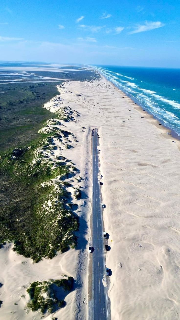 This may contain: an aerial view of the beach with cars driving on it and water in the background