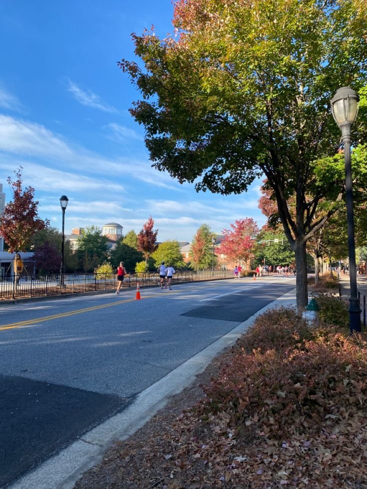 This may contain: people are jogging down the street on a sunny day with trees in the foreground