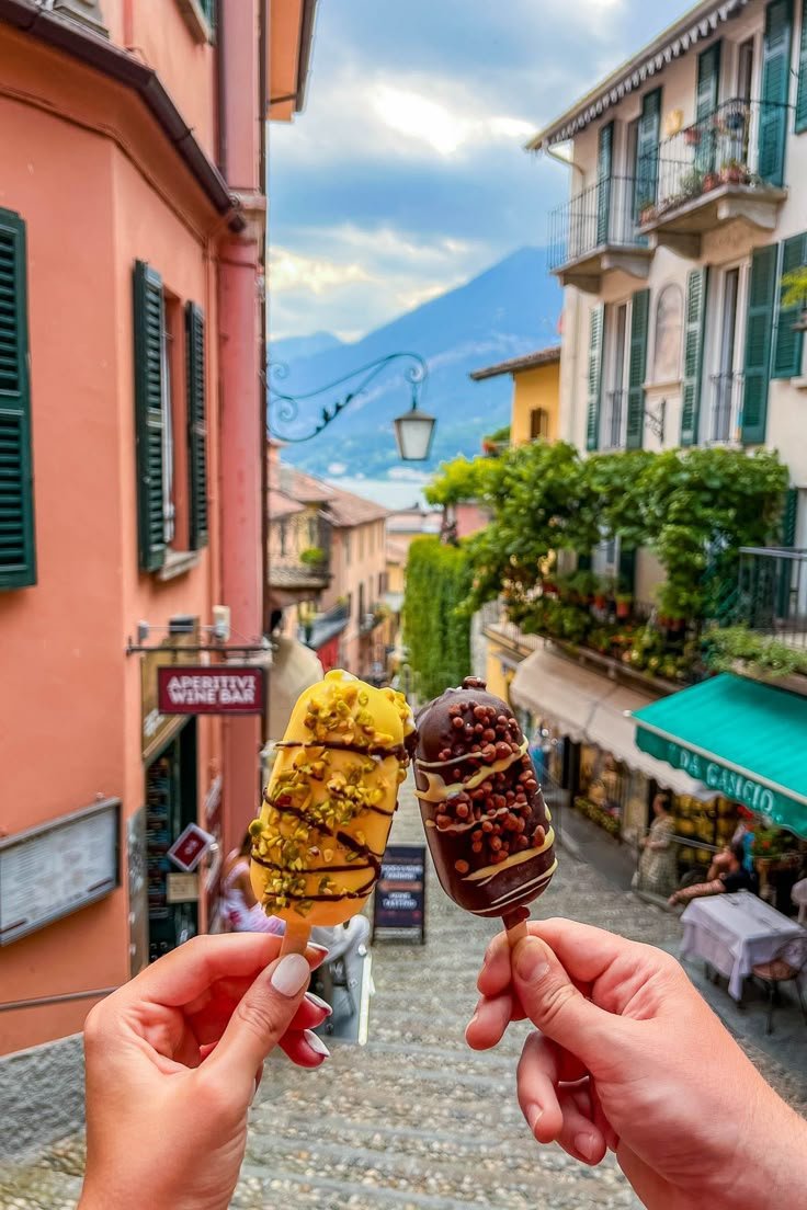 This may contain: two people holding ice cream cones in front of an alleyway with buildings on both sides