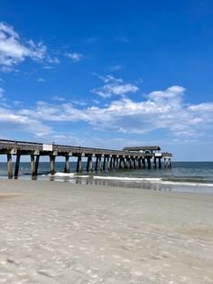 This may contain: a long pier stretches out into the ocean on a sunny day with blue skies and white clouds