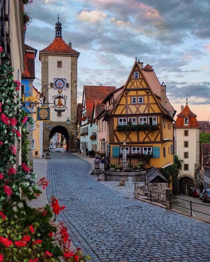 This may contain: an image of a street with buildings and flowers in the foreground, on a cloudy day