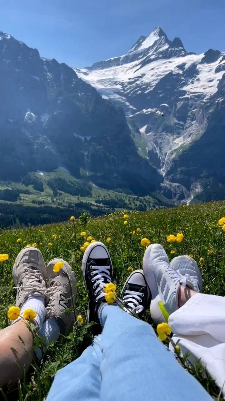 This may contain: two people sitting in the grass with their feet up