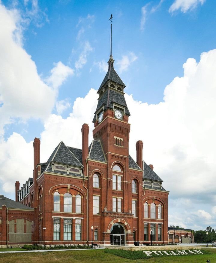 This may contain: an old red brick building with a clock tower on top and grass in the foreground