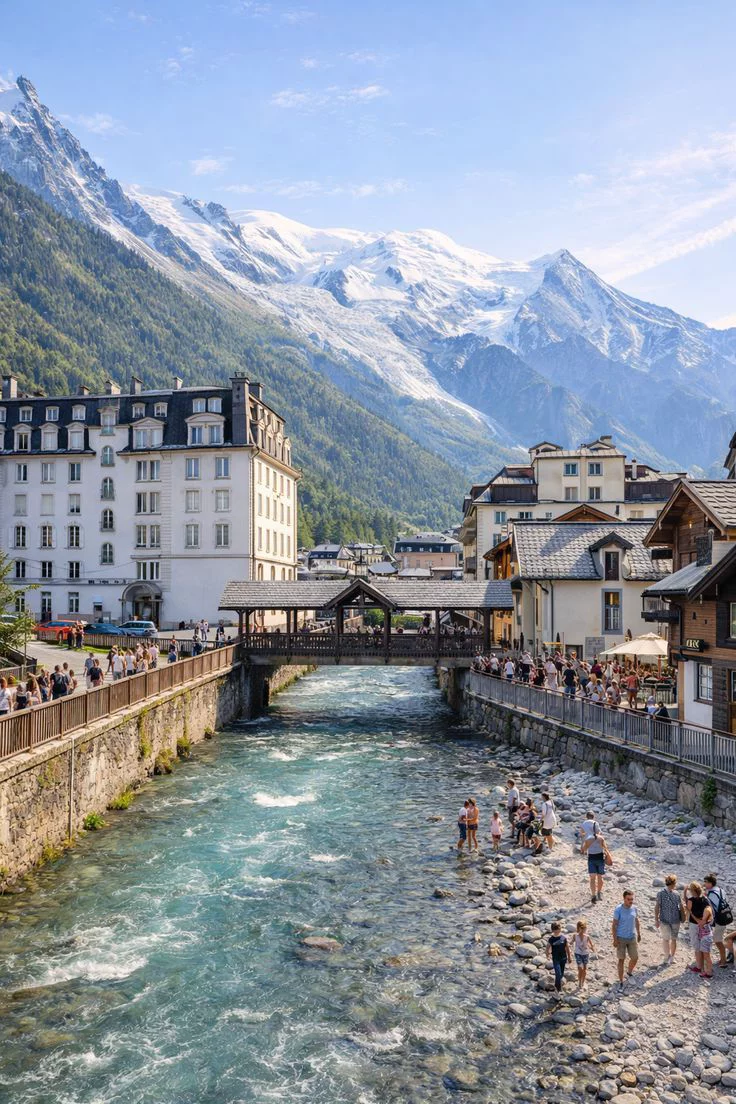 This may contain: people are standing on the side of a river next to buildings and mountains in the background