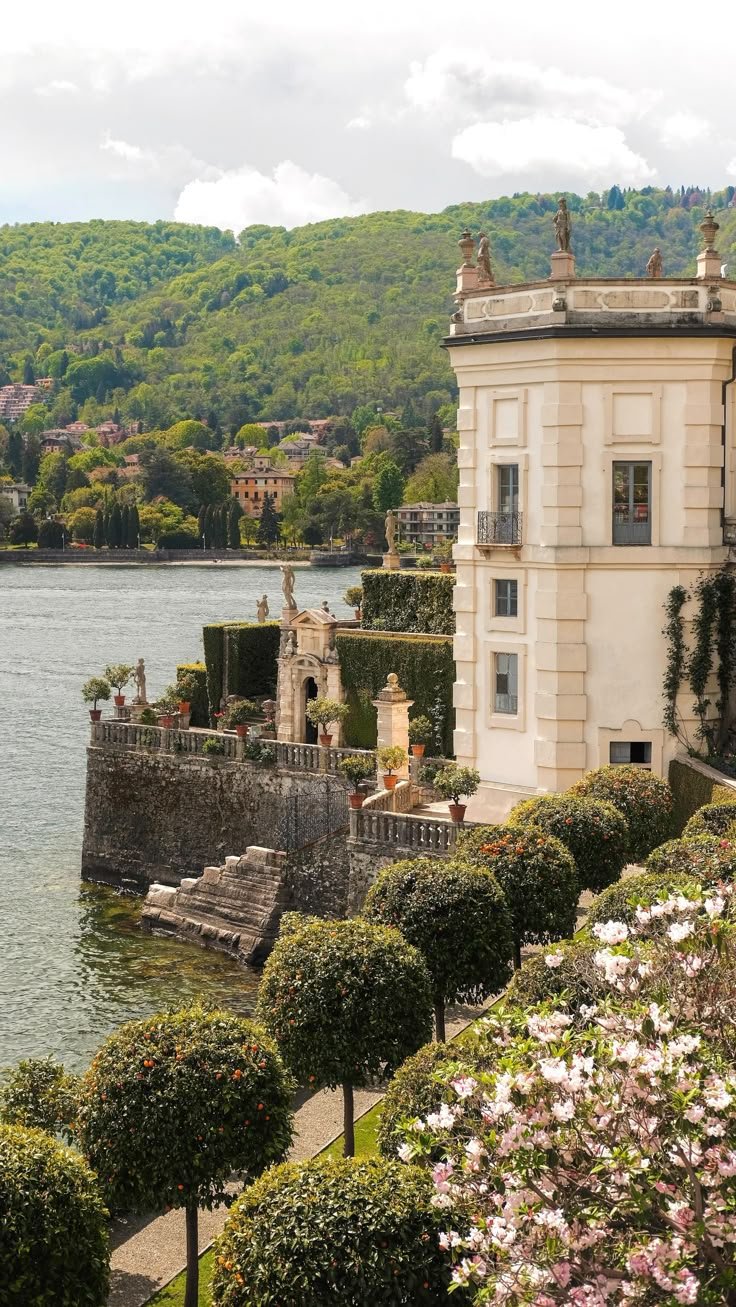 This may contain: a large building sitting on top of a lush green hillside next to a body of water