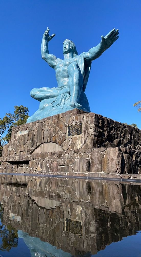 This may contain: a statue of a man sitting on top of a rock next to a body of water