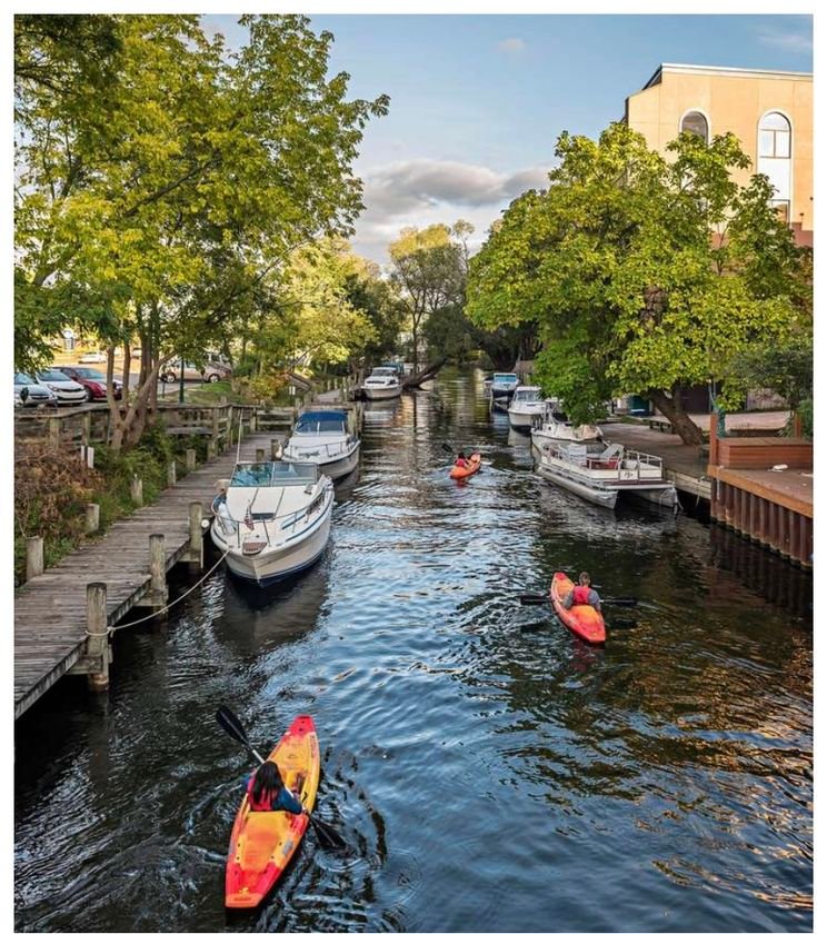 This may contain: there are many small boats on the water in this city canal that is lined with trees and houses
