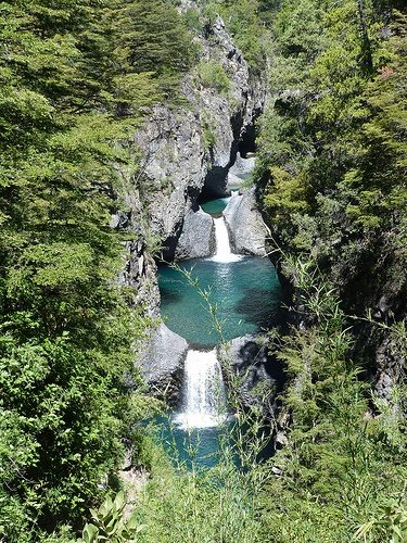 This may contain: there is a small waterfall in the middle of some trees and water that runs through it
